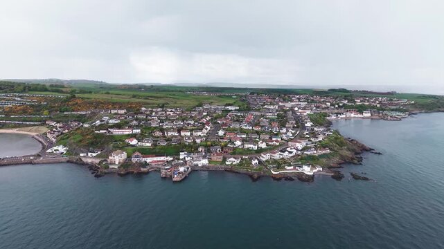 Aerial scenic panorama of Pettycur coastal settlement with houses on hillside and rocky shores, Fife, Scotland