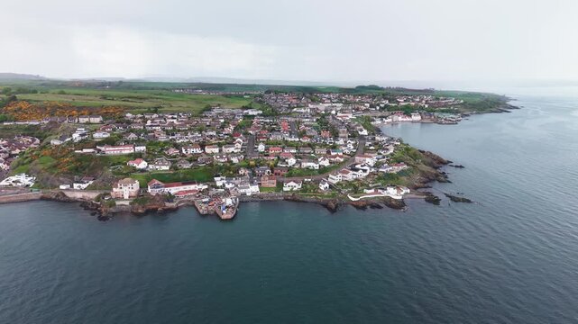 Aerial drone tracking shot capturing traditional coastal houses and rocky beach in Pettycur village, Fife, Scotland