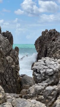 Turquoise Atlantic water swirling through a narrow rocky coastal channel between rugged ocean rocks under cloudy sky. Restless waves and natural coastal motion.