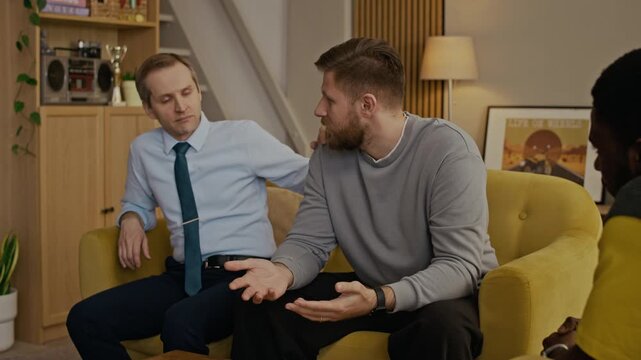 Medium shot of Caucasian man sitting on sofa, gesticulating in air while sharing emotions and feelings with best friends