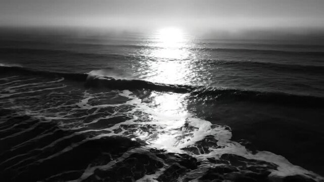 Black and white ocean waves crashing at sunset creating a mesmerizing seascape with sun reflection