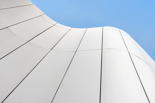 Abstract view of a modern white building facade with smooth curved panels and strong vertical lines, evoking minimalism, calm and contemporary architectural design against a clear blue sky