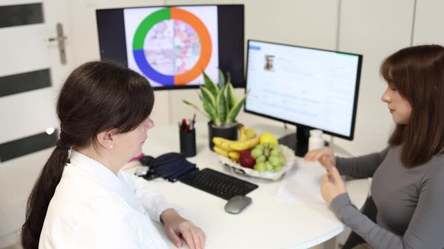 Young woman visits nutrition specialist to learn healthy eating habits while doctor explains balanced diet with fresh fruits and wellness chart during lifestyle consultation