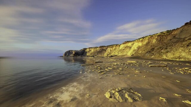 wide vista of eroded Paracas cliffface showing layered strata, exposed outcrops, sediment bands and rocky talus under soft sky with distant calm sea