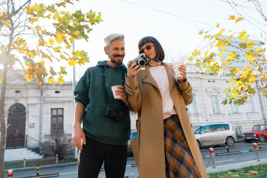 Couple exploring the city with cameras and coffee on a sunny autumn street