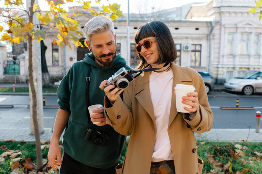 Friends exploring the city: smiling photographers with coffee and a camera on an autumn street