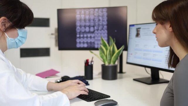 Healthcare consultation in modern clinic doctor working with patient records while young woman waits for diagnosis and professional medical recommendations
