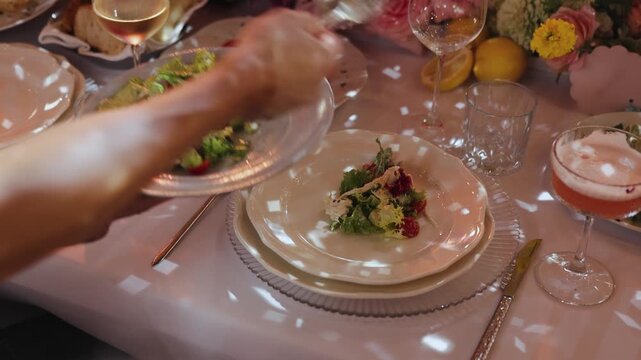 Unrecognizable waiter serving salad onto guest plate in slow motion at luxury wedding banquet. Anonymous caterer placing gourmet food at restaurant dinner. Elegant hospitality. 4K stock footage.
