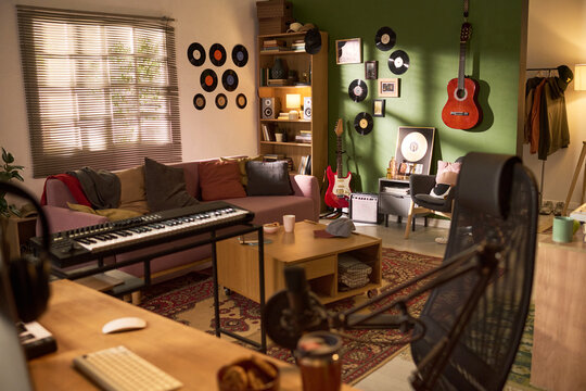 Wide angle shot of home music studio featuring keyboard, guitars, microphone, sofa, vinyl decor, supporting content creation, podcast production, musician branding, creative workspace marketing