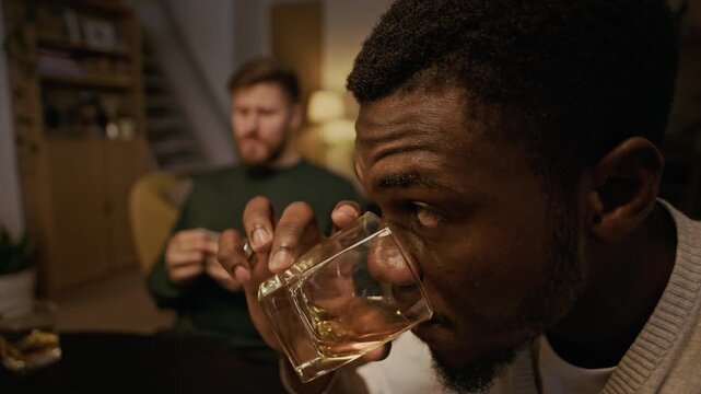 Close up of African American man taking sip of bourbon and looking at hand while playing poker with friends