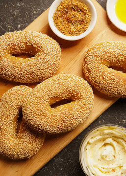 Homemade gluten free ka'ak al Quds, also known as Jerussalem bagels. Featuring oval shaped bagels covered with toasted sesame seeds, served with mixed spices, on a wooden board.