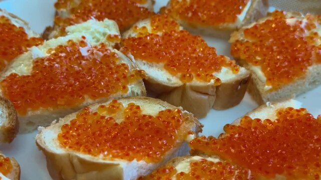 Red caviar sandwiches on plate close-up butter spread on white bread arranged on festive table with ceramic plate and spoon warm