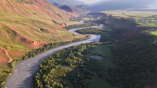 Wide aerial of Naryn River winding through valley with colorful eroded hills at golden hour, Kyrgyzstan