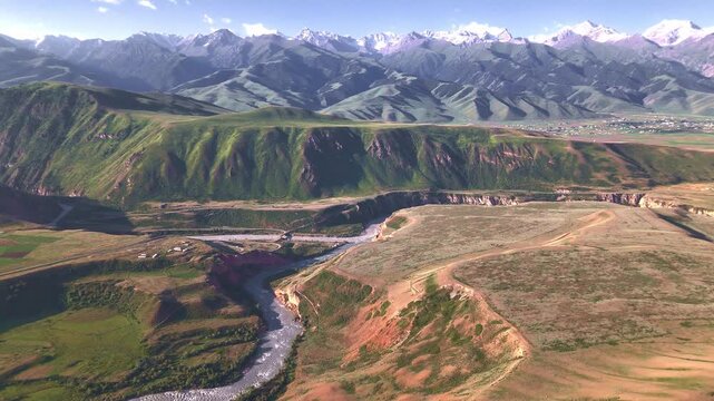 Wide aerial panorama of Naryn River gorge with eroded cliffs and Tian Shan snow peaks, Kyrgyzstan