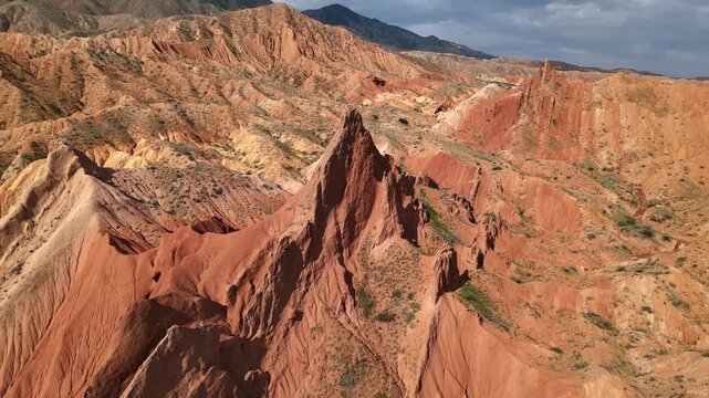 Drone orbiting jagged red rock towers of Skazka Canyon revealing colorful layered hills, Kyrgyzstan