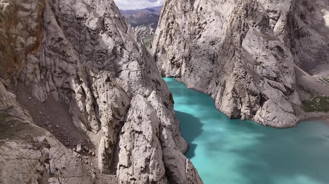 Aerial drone flight through Kol-Suu Lake canyon, Kyrgyzstan - turquoise water between towering rock cliffs