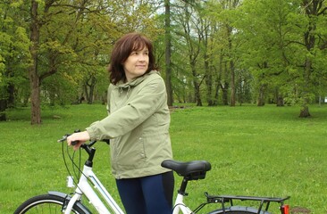 Obraz premium Radiant woman posing with bicycle outdoors in a summer park, concept of active lifestyle and freedom.