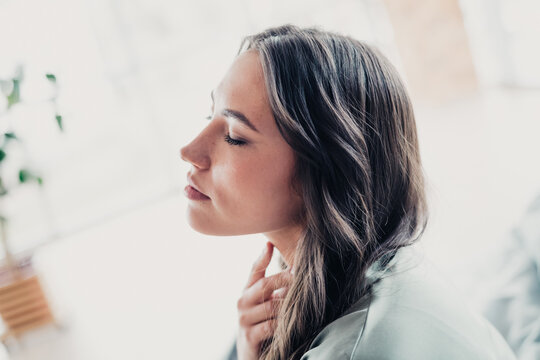 Young woman relaxing with eyes closed, hand at throat, pensive calm portrait in soft natural light