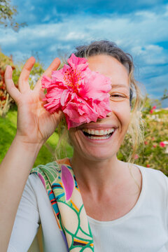 Smiling woman holding pink hibiscus flower over eye