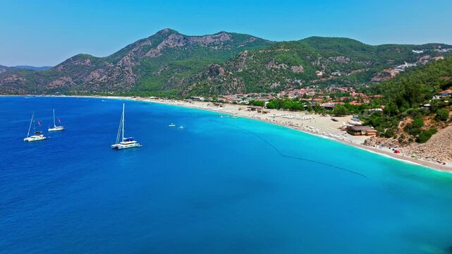 Aerial view of Oludeniz Beach, Turkey coastline and bay. Boats and ships float on blue water near steep cliffs and green mountains.