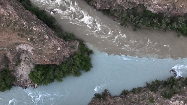 Drone flying through deep Boom Gorge above raging Chu River with red rock walls, Kyrgyzstan