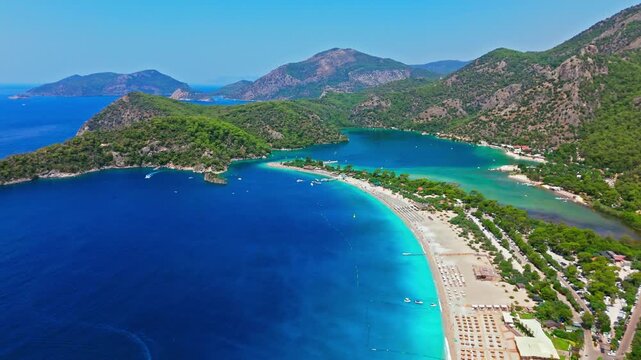 Drone view of Oludeniz Beach, Turkey curved coastline. Blue water, sandy shore, green hills and mountains create a famous travel scene.