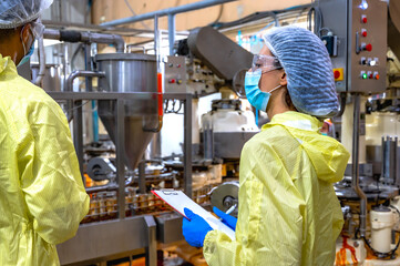 Fototapeta premium Expertise man and woman food safety inspectors in hairnets and gowns inspecting canning process at modern manufacturing plant