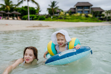 Obraz premium Sisters playing in shallow tropical sea during family beach vacation.