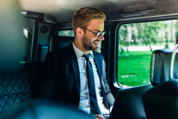 Handsome young businessman using laptop inside luxury car, side view of focused male executive in formal suit working remotely, business travel and modern corporate lifestyle theme © InsideCreativeHouse