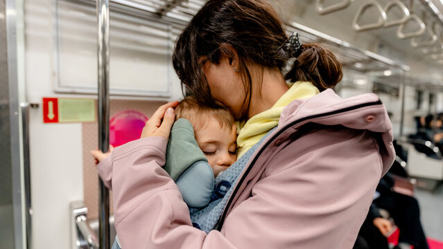 Mother comforting sleeping toddler on subway during travel