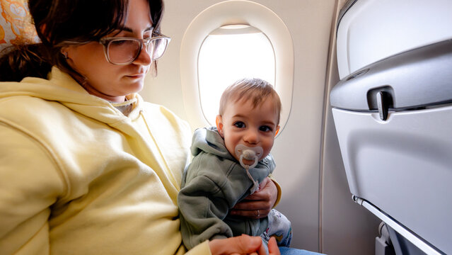 Mother holding baby on airplane seat during family travel