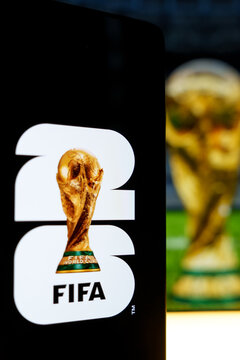 Official FIFA World Cup 2026 brand logo displayed on a digital screen alongside a blurred trophy background, concept of international soccer tournament and football championship merchandise in the USA