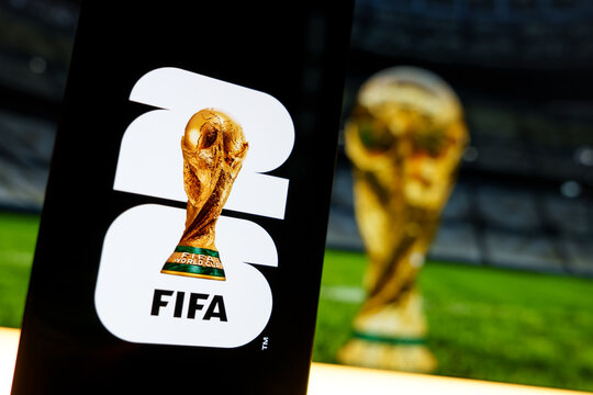 Official FIFA World Cup 2026 brand logo displayed on a digital screen alongside a blurred trophy background, concept of international soccer tournament and football championship merchandise in the USA