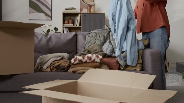 Tilt down view of African American girl examining blue shirt, taking it off hanger and tossing into cardboard box while sift through clothes at home