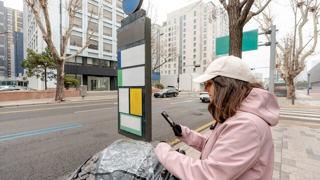 Mother with stroller at a Seoul bus stop using smartphone