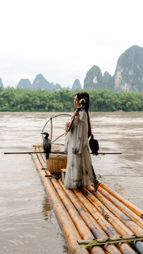 Hanfu girl with cormorants on bamboo raft in Xingping