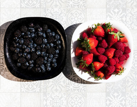 Fresh berry assortment in bowls on patterned tile background