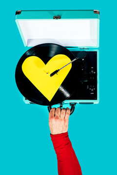 Hand holds retro record player with heart vinyl on turquoise backdrop