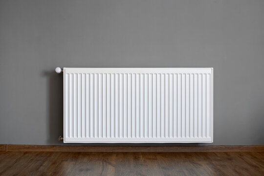 Close-up of a bimetallic heating radiator in an apartment against a grey wall and wooden floor.