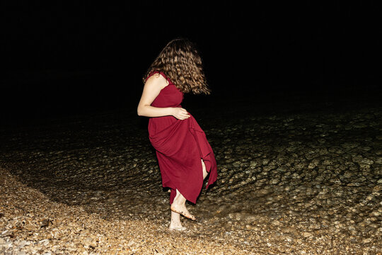 Woman in red dress stepping in water at night beach