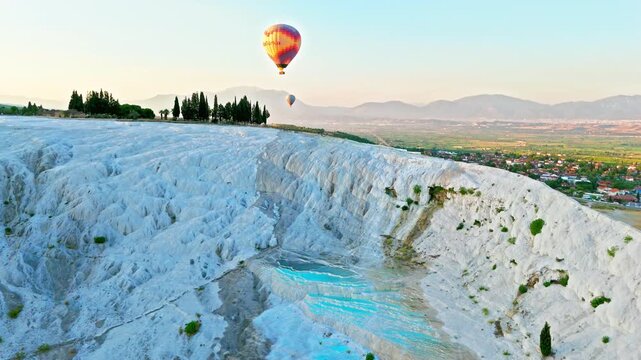 Aerial view of Travertines of Pamukkale, Turkey. Hot air balloon floats over white limestone terraces and natural thermal pools at sunrise.