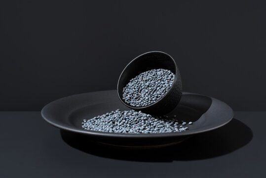 Black beluga lentils spilled from bowl on dark plate