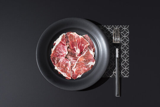Top view of acorn-fed Spanish cured ham on black plate