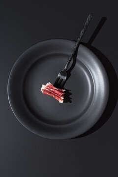 Minimalist plate with fork holding sliced Spanish cured ham