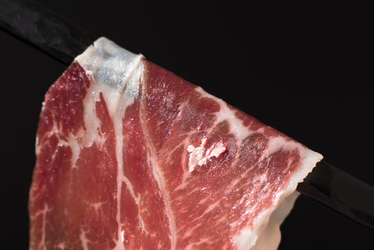 Iberian cured Spanish ham slice on dark background