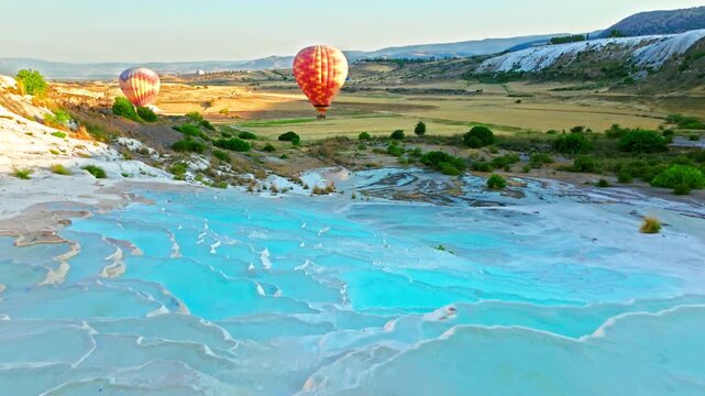 Drone view of Travertines of Pamukkale, Turkey. Hot air balloon floats above natural thermal pools and white limestone terraces at sunrise.