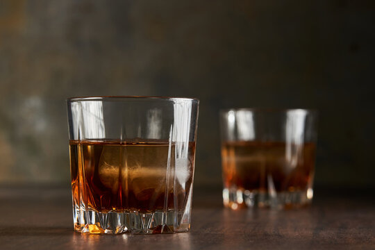 Glass of whisky bourbon with ice on rustic bar table