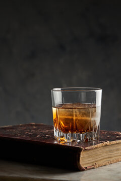 Glass of bourbon whisky on old book with dark background