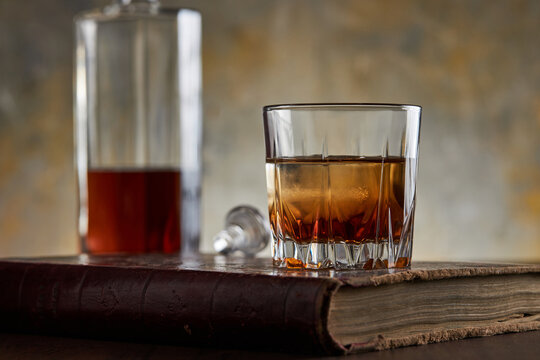 Whisky bourbon on rocks in glass with bottle on book