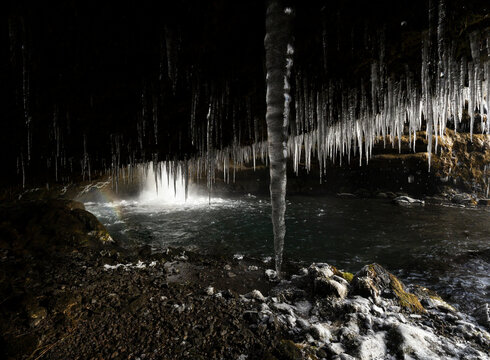 Iceland winter waterfall inside cave with icicles and spray